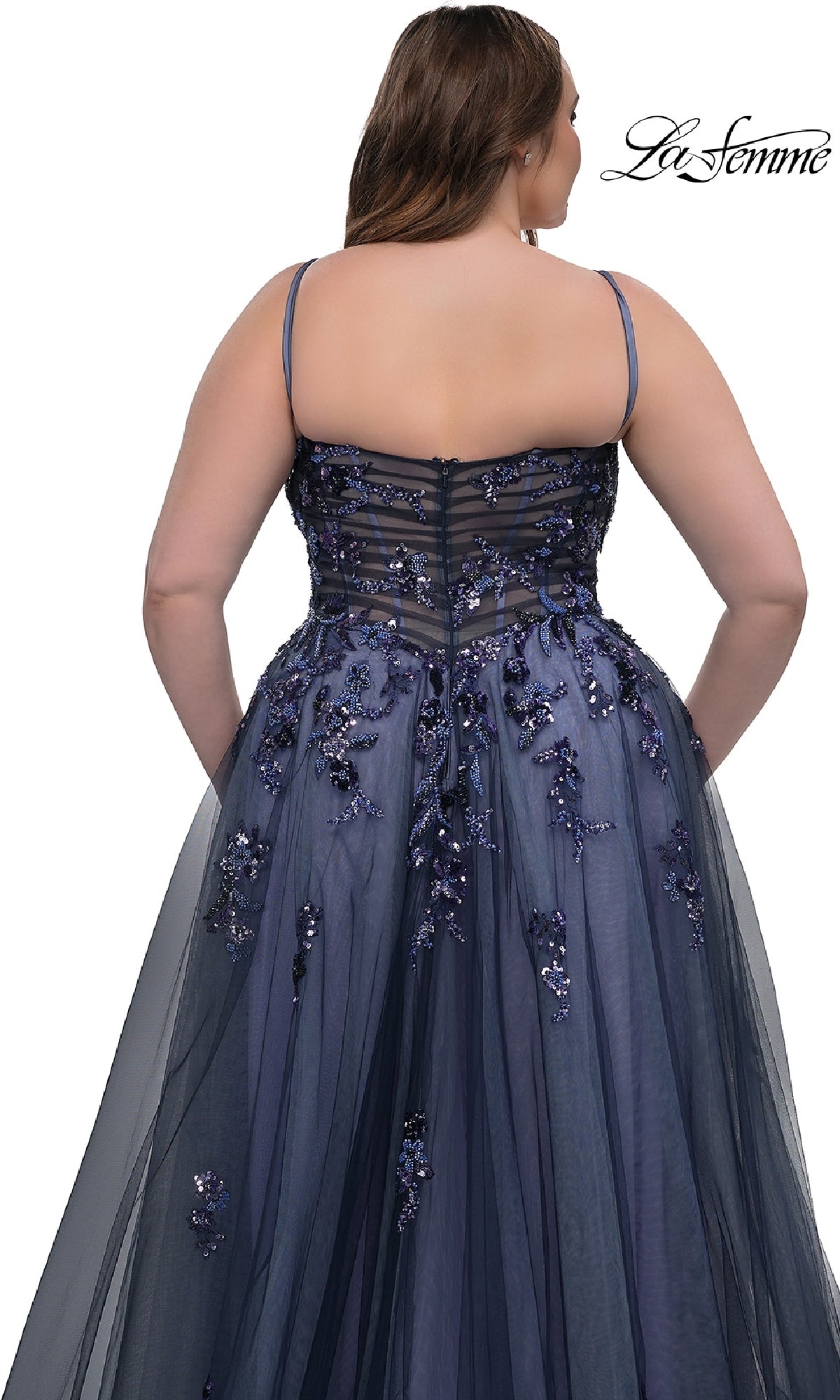 A woman in the Navy Plus-Size Prom Dress: La Femme 33061, featuring sequin floral applique and thin straps, stands facing away to highlight the elegant back detailing and flowing A-line skirt.